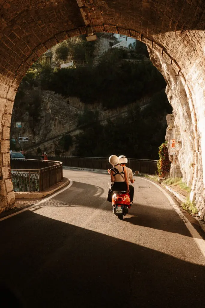 Paar auf einem roten Roller, das durch einen Torbogen in Amalfi fährt