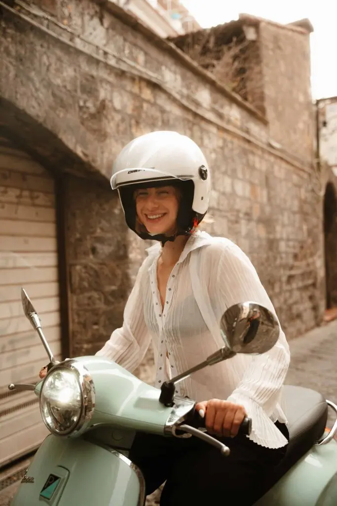 Frau mit Helm, die auf einer mintgrünen Vespa an der Amalfiküste lächelt