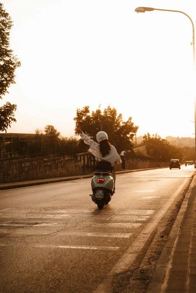 woman on a scooter with arm raised at sunset in Amalfi