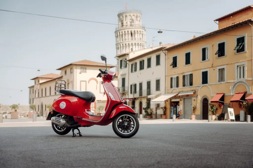 rote Vespa, die auf einer Piazza mit dem Schiefen Turm von Pisa geparkt ist