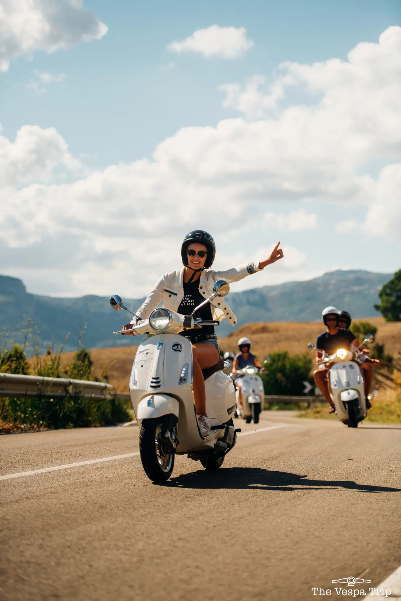 Gruppe von Menschen, die auf einer sonnigen Straße in Sizilien weiße Vespas fahren