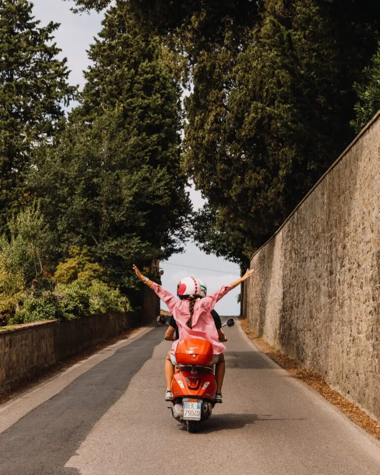 Frau auf dem Rücksitz eines Rollers mit ausgebreiteten Armen in der Toskana