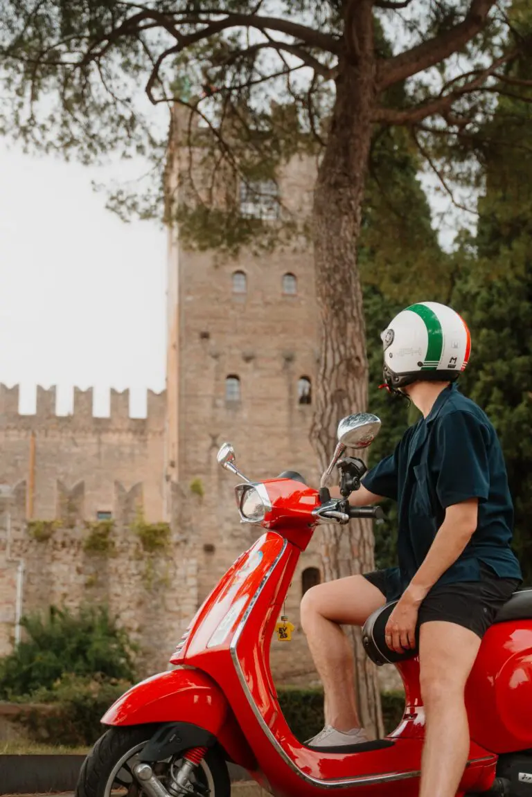 Person auf rotem Vespa-Roller vor einer historischen italienischen Burg