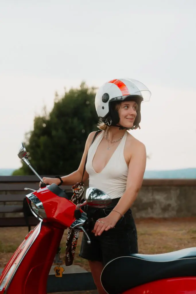 junge Frau mit Helm auf rotem Vespa-Roller