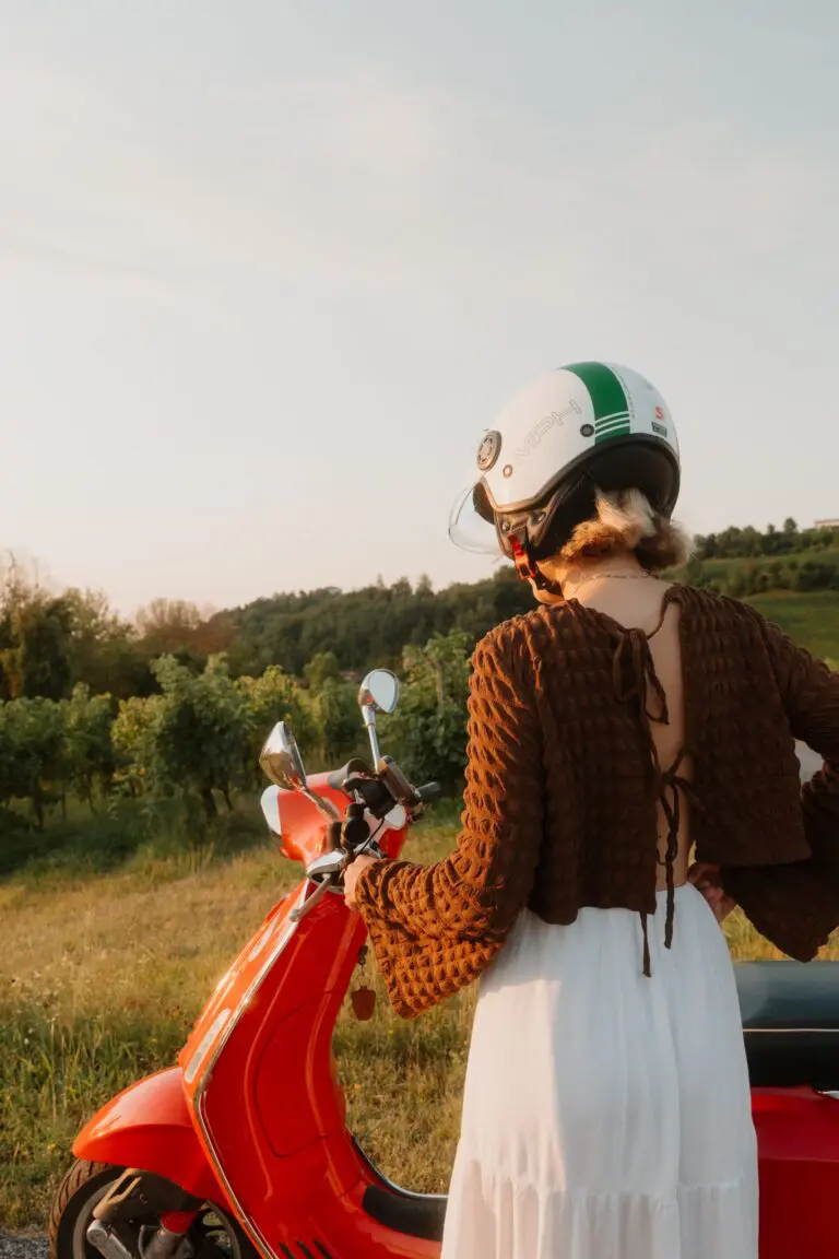 Frau mit Helm auf roter Vespa in einem Weinberg in Venetien bei Sonnenuntergang