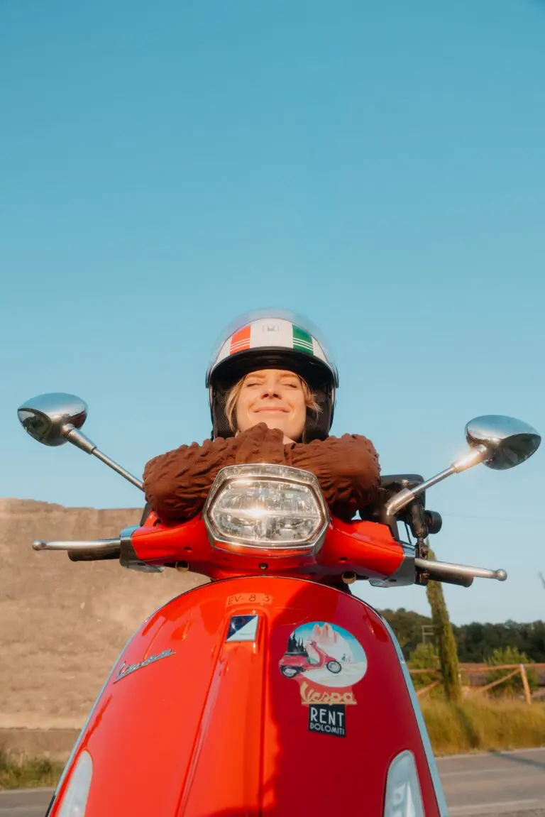 Frau mit Helm auf rotem Vespa-Roller in Venetien