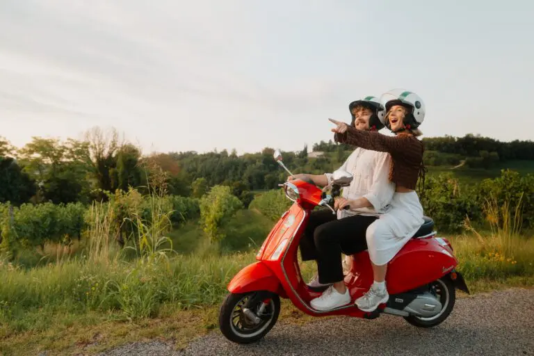 Paar fährt bei Sonnenuntergang mit einer roten Vespa durch die Weinberge Venetiens