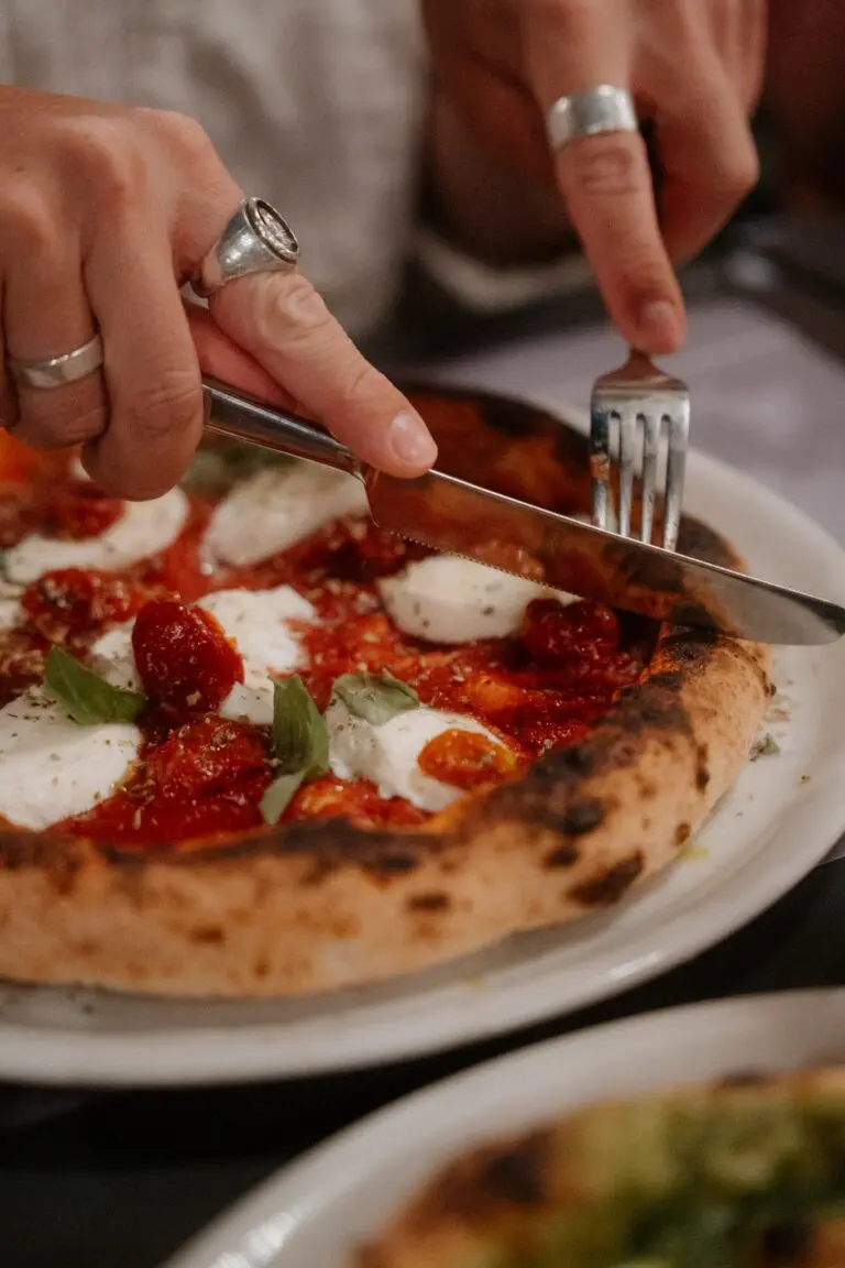 Hände, die eine frische Pizza mit Mozzarella und Basilikum schneiden