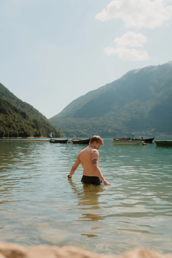 man wading in a lake with mountains and boats