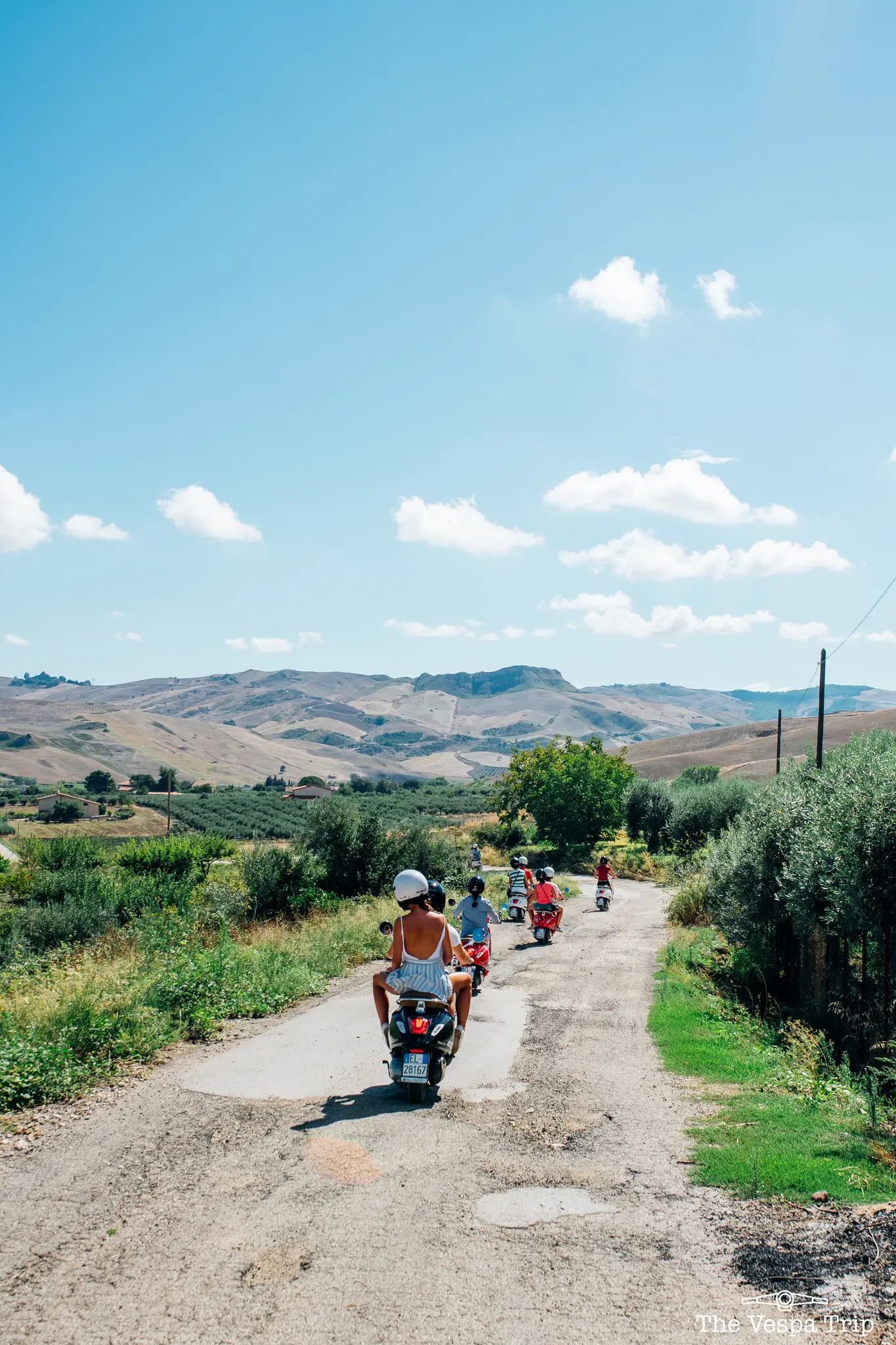 Eine Gruppe von Menschen fährt mit Vespas auf einer Landstraße in Sizilien.