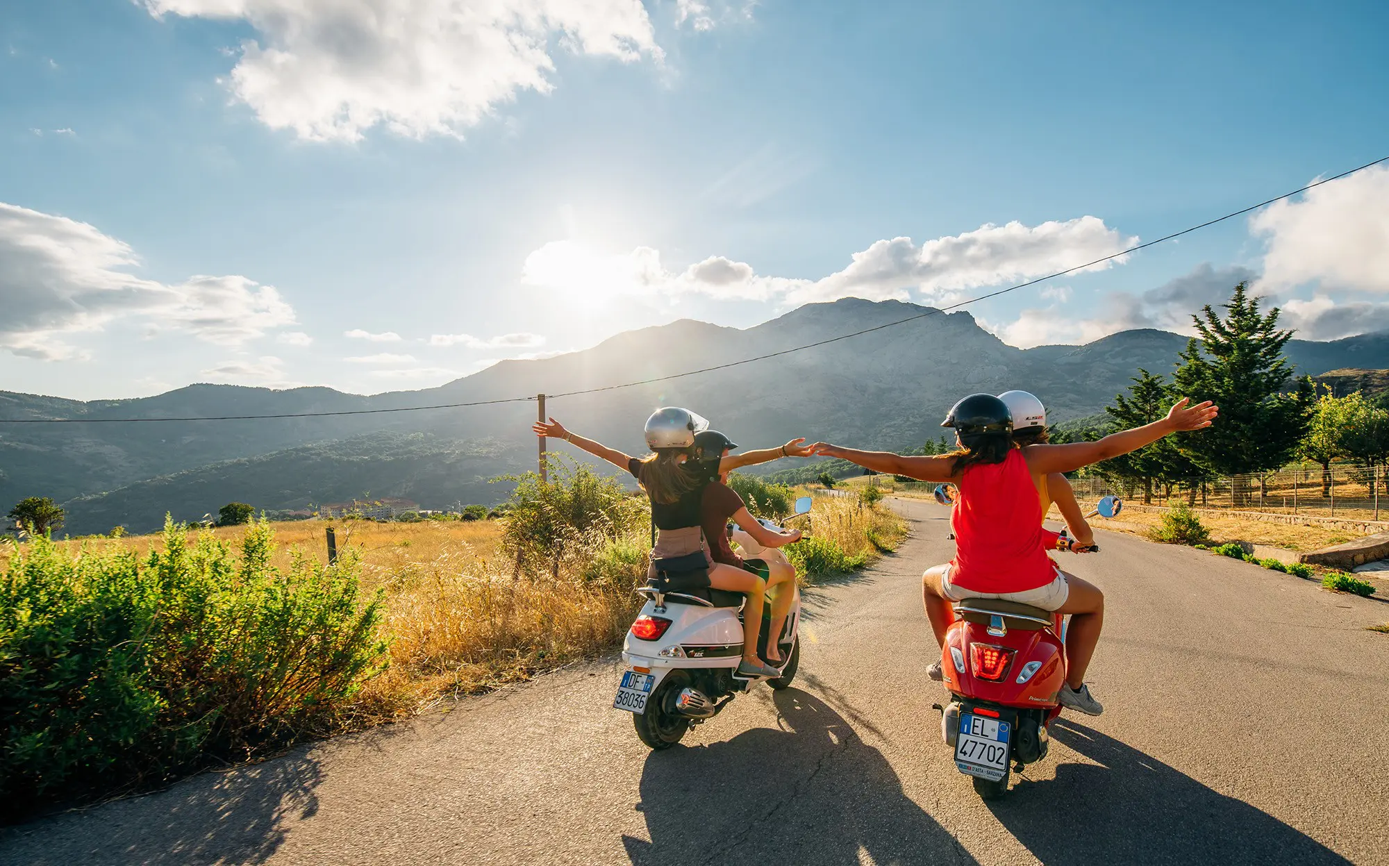 Freunde fahren mit Vespas über eine malerische Straße auf Sizilien