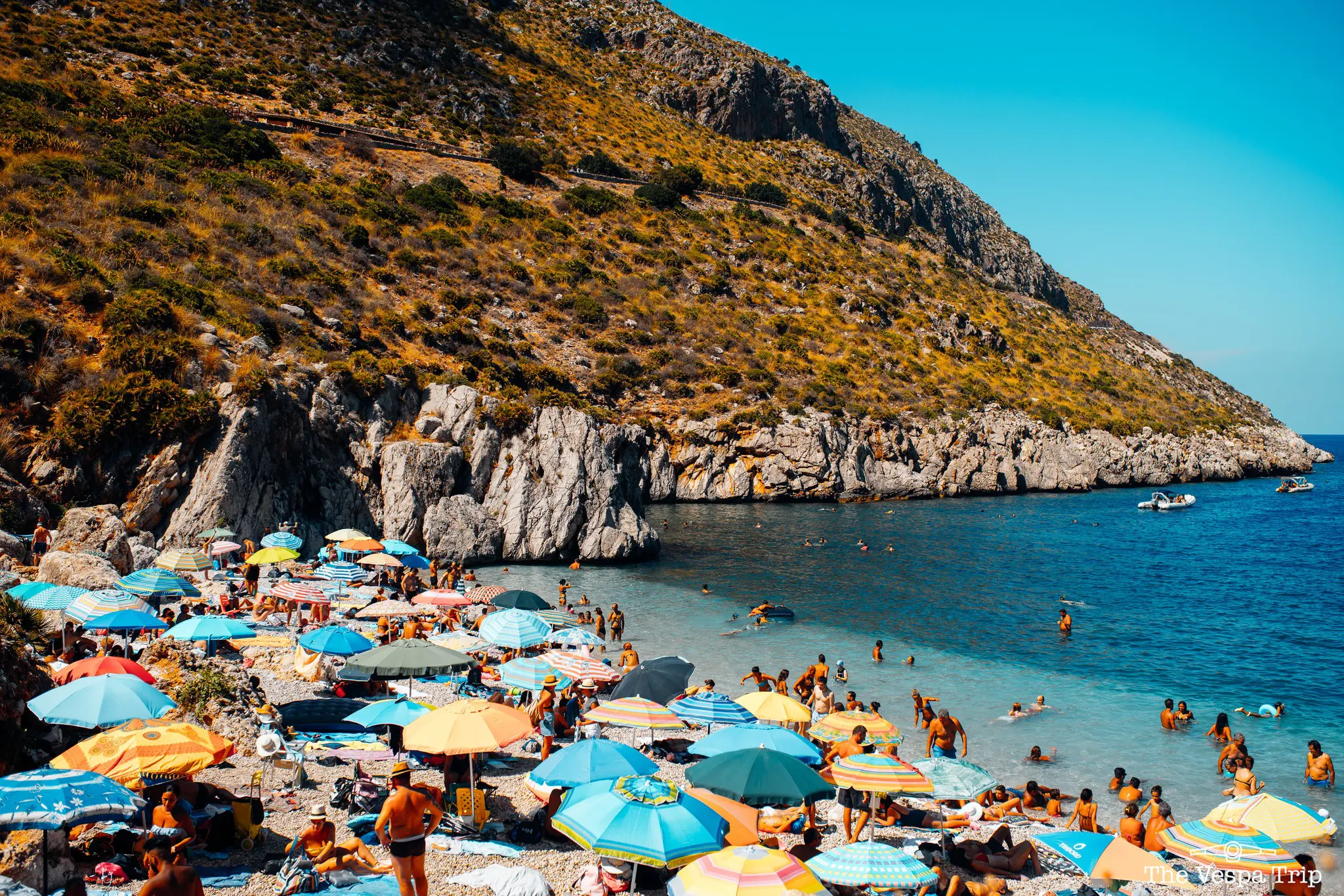 belebter Strand mit bunten Sonnenschirmen und Menschen, die in Sizilien schwimmen
