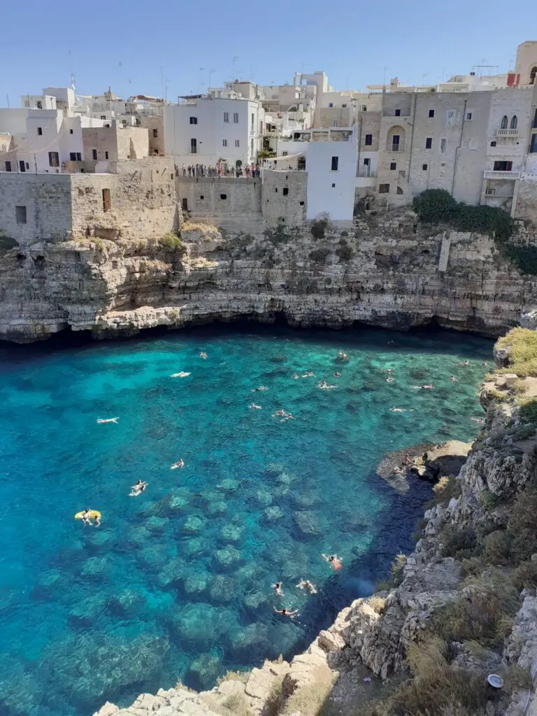 Klippenstadt Polignano a Mare mit Menschen, die im türkisfarbenen Wasser schwimmen