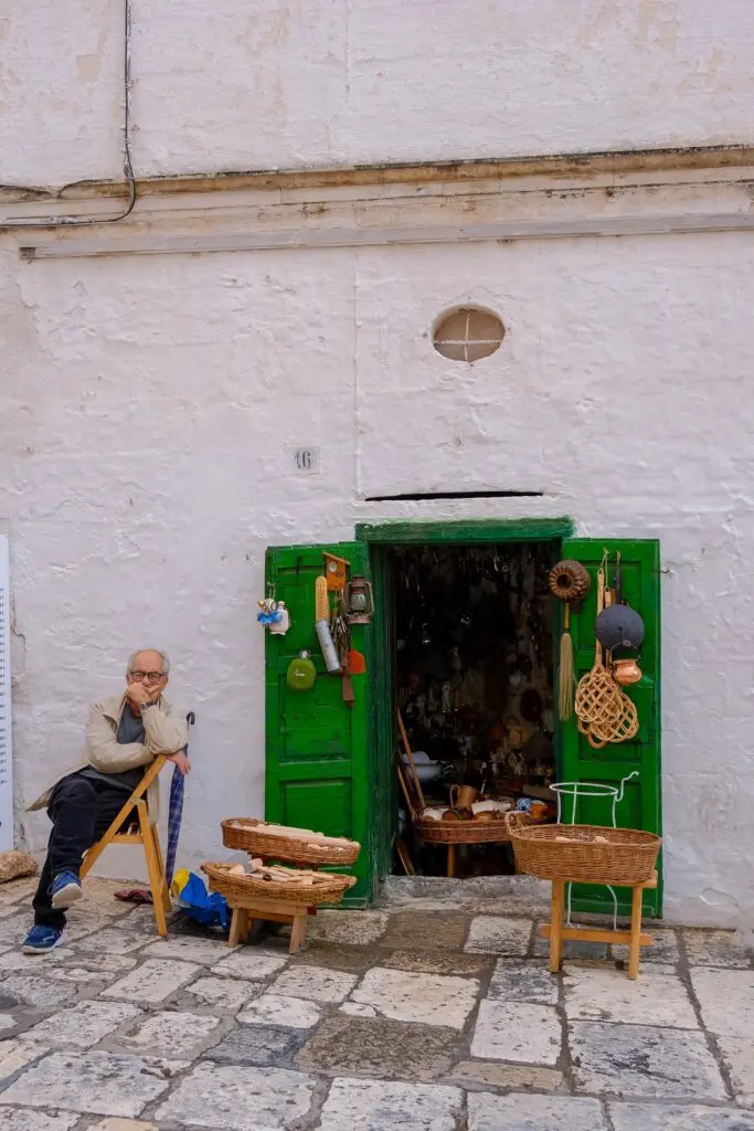 Mann sitzt vor einem Geschäft mit grünen Türen in Ostuni, Apulien