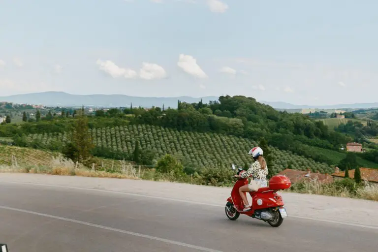 Frau fährt mit roter Vespa durch die toskanische Landschaft