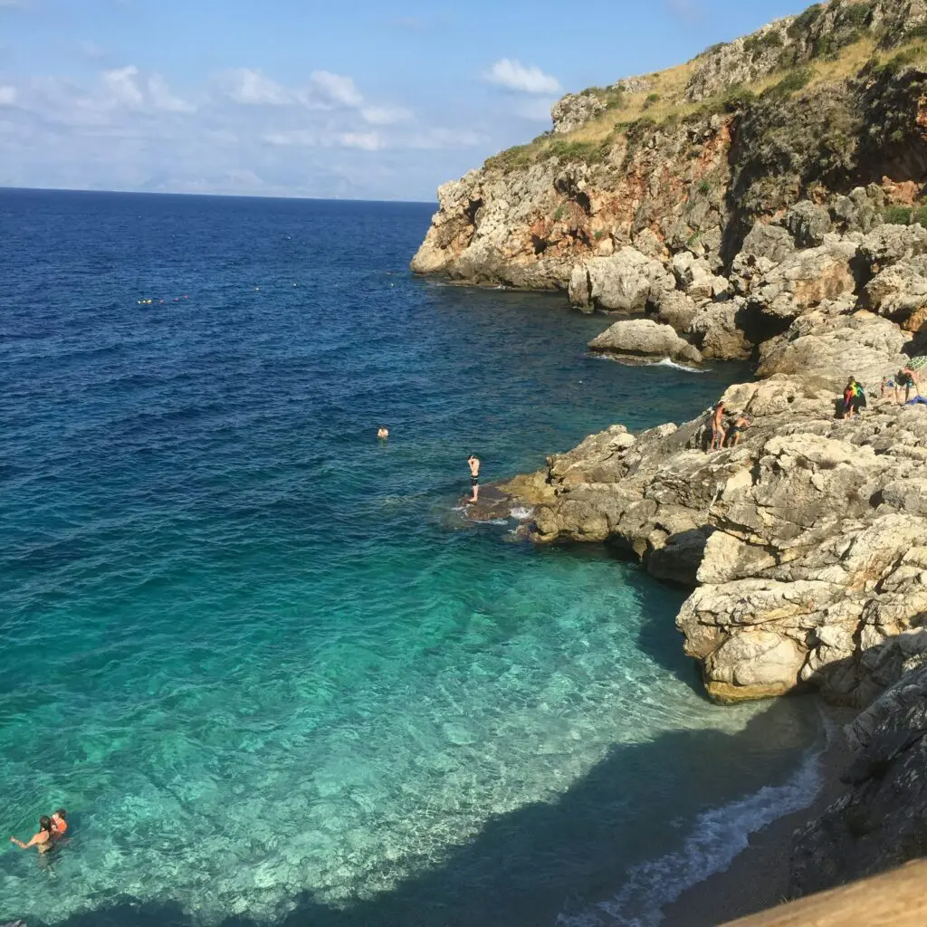 people swimming on sea near rocky mountain during daytime