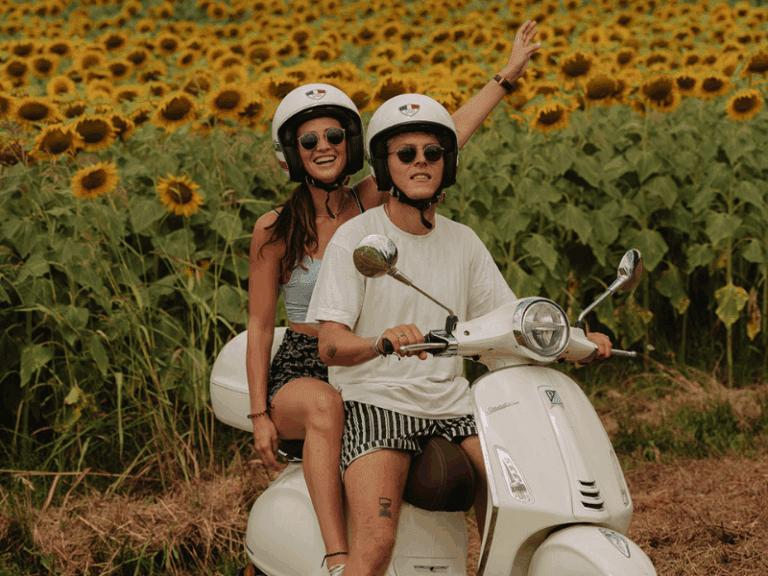 Paar auf einer weißen Vespa Primavera mit Sonnenblumen im Hintergrund