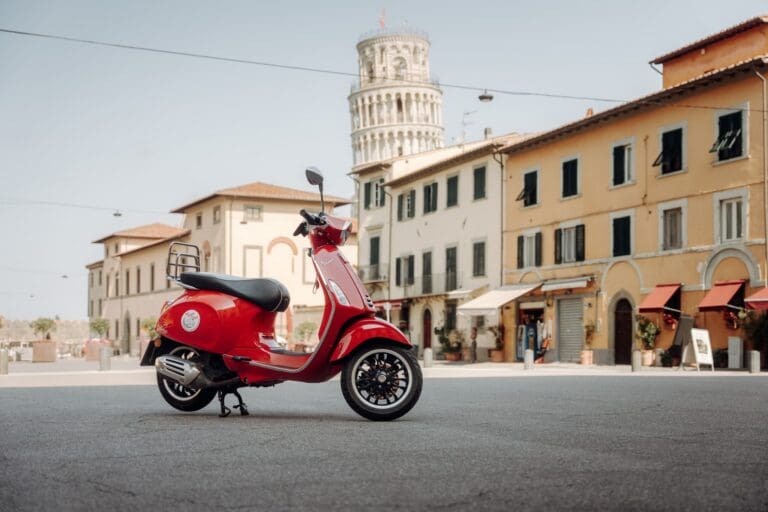 rote Vespa, die auf einer Piazza mit dem Schiefen Turm von Pisa geparkt ist