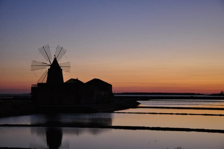 Silhouette einer Windmühle bei Sonnenuntergang über den Salinen von Marsala, Sizilien