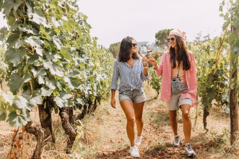 two women walking through a vineyard toasting with wine