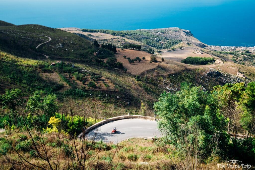 rote Vespa auf einer kurvigen Straße mit Blick auf das Meer in Sizilien